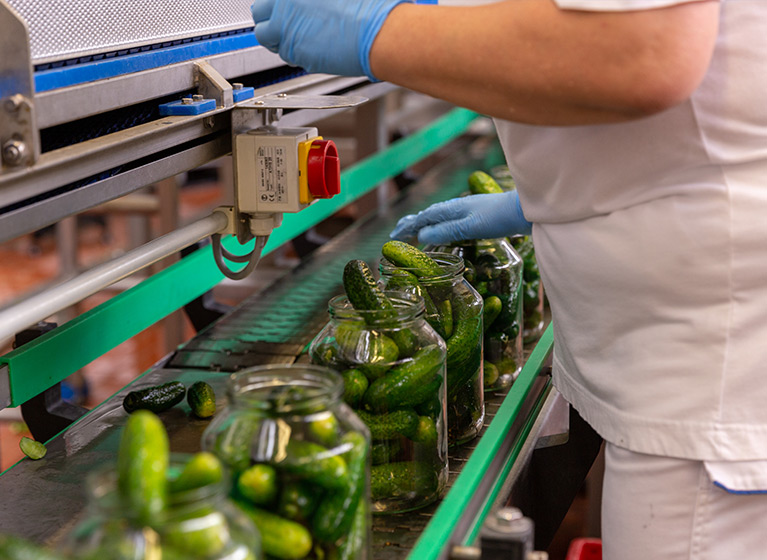 Jars of gherkins getting refilled by hand.