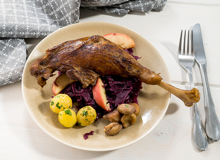 A white plate with goose leg and red cabbage.