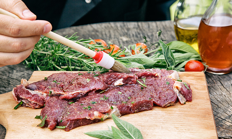 A person putting marinade on a piece of meat.